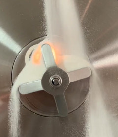 A mechanism for representative powder presentation in front of a sensor (illuminated in the background). Image courtesy of Acuitis Process Analytics Ltd & Expo Process Analytics Ltd. 
